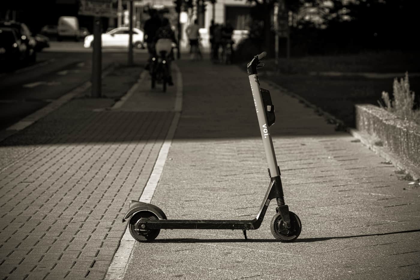 An electric scooter standing on a paved path beside a park