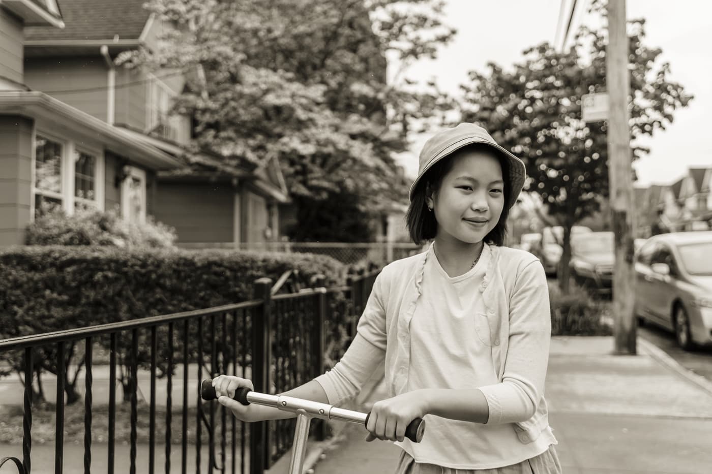 A teenager standing beside an electric scooter on a residential street